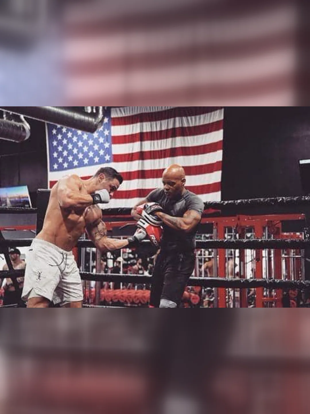 Coach Bizz holding pads for his fighter in the ring, under the flag